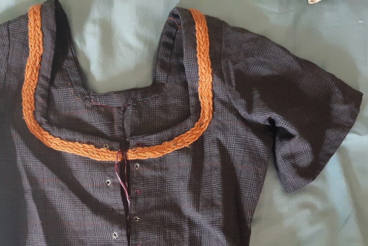 Close-up of a dark grey gown with short sleeves and orange woven trim along the neckline.